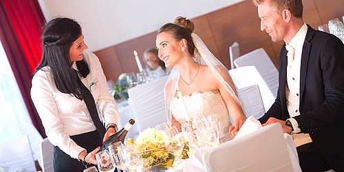 [Translate to English:] Hochzeitspaar mit Catering Bedienung